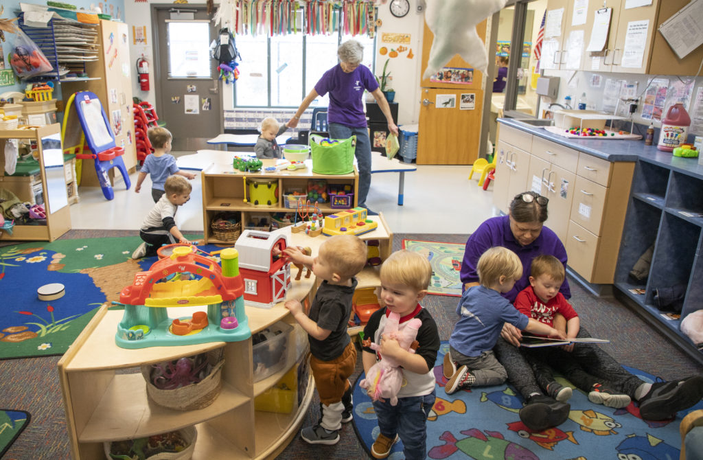 Two child care instructors tend to a room filled with young children.