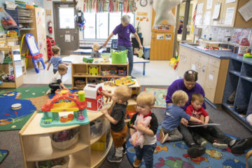 Two child care instructors tend to a room filled with young children.